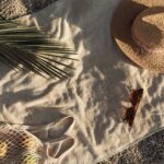 Ein Handtuch mit Logo liegt am Strand neben einem Strohhut und einer Sonnenbrille – das ideale Werbemittel für sonnige Tage.