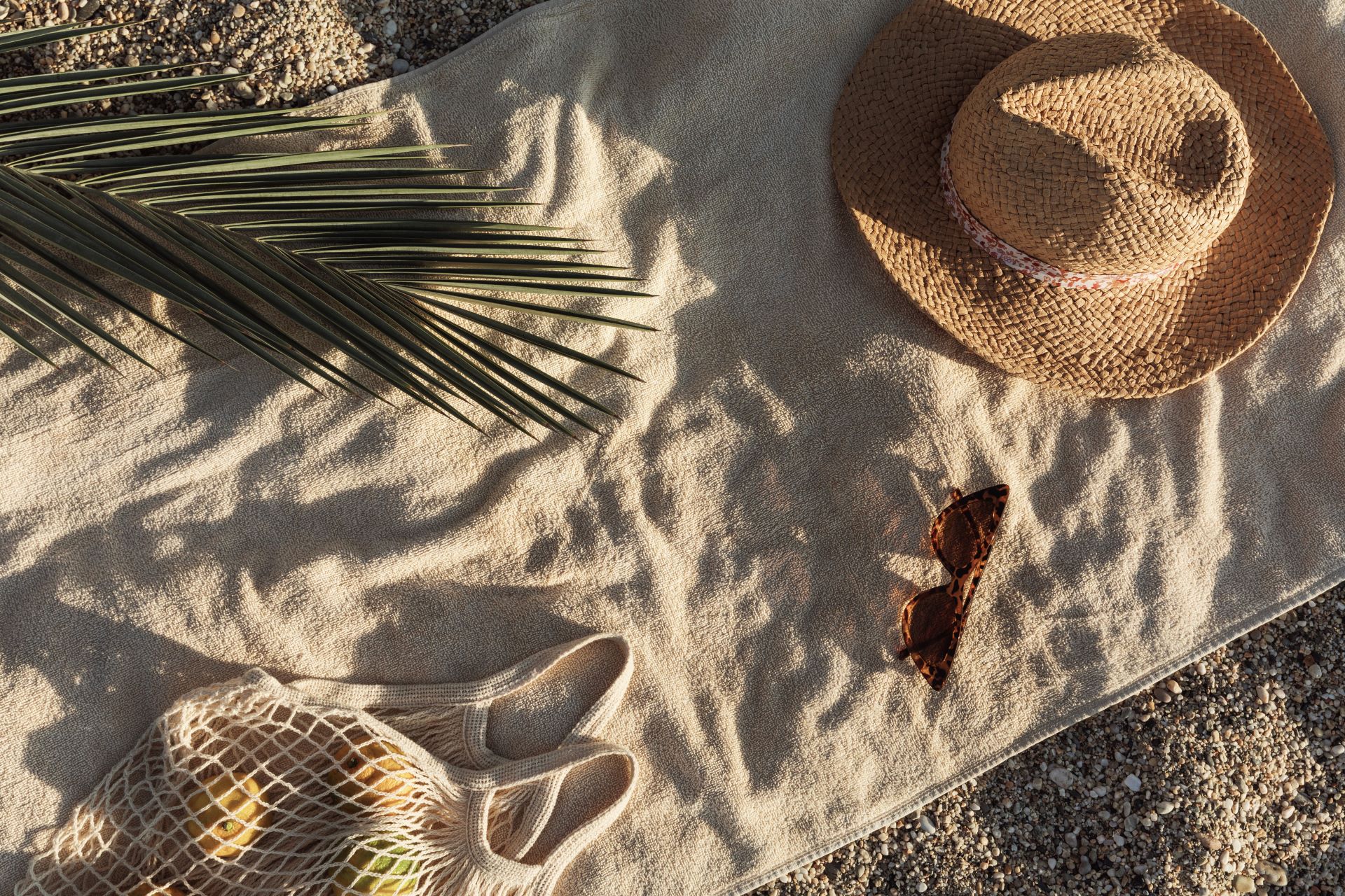 Ein Handtuch mit Logo liegt am Strand neben einem Strohhut und einer Sonnenbrille – das ideale Werbemittel für sonnige Tage.